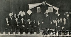 1933, Buenos Aires, Argentyna.
Marszałek Sejmu RP Władysław Raczkiewicz przemawia podczas spotkania z Polonią argentyńską. Na scenie również: p. Bernstein (siedzi 2. z lewej), p. Ciapciak (siedzi 3. z lewej), p. Jahilnicki (siedzi 2. z prawej), Stanisław Pyzik (siedzi 1. z lewej), prezes Związku Polaków w Argentynie Franciszek Marus (siedzi 4. z lewej),  p. Pikulski (siedzi w głębi. 2. z lewej od W. Raczkiewicza), prezes organizacji polonijnej w Dock Sud p. Pleśniak (siedzi w głębi. 1. z lewej od W. Raczkiewicza),  Juliusz Nowiński z Banco Polaco (siedzi 1. z prawej), Rudolf Friedenberg (siedzi 3. z prawej), Zygmunt Zach (siedzi 4. z prawej), p. Prochownik (siedzi 5. z prawej). 
Fot. NN, zbiory Biblioteki Polskiej im. Ignacego Domeyki w Buenos Aires (Biblioteca Polaca Ignacio Domeyko)