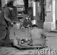 Lata 60., Warszawa, Polska.
Chłopiec z karabinem-zabawką przygląda się pracy monterów przy studzience kablowej.
Fot. Marek Zürn, zbiory Fundacji Ośrodka KARTA