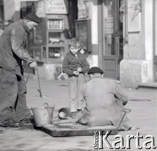 Lata 60., Warszawa, Polska.
Chłopiec z karabinem-zabawką przygląda się pracy monterów przy studzience kablowej.
Fot. Marek Zürn, zbiory Fundacji Ośrodka KARTA