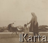 1900-1920, miejsce nieznane.
Spacer drogą wzdłuż morza. Kobieta prowadzi wózek, za który trzyma też dziewczynka. W tle widać łódki.
Fot. NN, kolekcja rodziny Walińskich, zbiory Fundacji Ośrodka KARTA