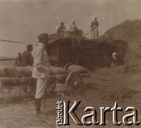 1900-1920, miejsce nieznane, Polska.
Młócenie. Chłopki i chłopi podczas pracy. Odzielają ziarna od słomy przy pomocy maszyny. Na pierwszym planie stoi mężczyzna. Obok niego wóz, na którym leżą worki z ziarnem.
Fot. NN, kolekcja rodziny Walińskich, zbiory Fundacji Ośrodka KARTA