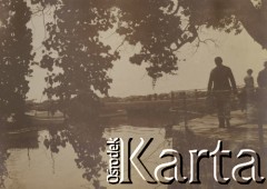 1900-1920, miejsce nieznane.
Przystań. Chodnikiem spacerują ludzie. Na wodzie zacumowały łódki. Zdjęcie zrobiono zza gałęzi drzew.
Fot. NN, kolekcja rodziny Walińskich, zbiory Fundacji Ośrodka KARTA