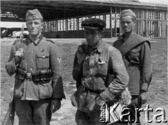 Lato 1941, Smoleńsk, ZSRR.
Obóz jeniecki, czerwonoarmiści i wartownik żołnierz Wehrmachtu, w hangarze, w głębi z lewej, stoi samolot typu Fi 156 