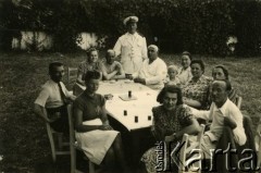 1940, Rumunia.
Polscy uchodźcy w Rumunii podczas II wojny światowej - grupa osób w letnich ubraniach siedzi przy stole, drugi od lewej: Tadeusz Krajewski; na odwrocie pieczęć: 