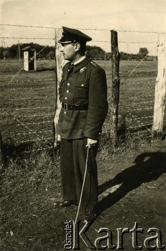 1940, Rumunia.
Kpt. pilot Tadeusz Krajewski w mundurze pilota stoi przy zasiekach z drutu kolczastego; na odwrocie pieczęć: 