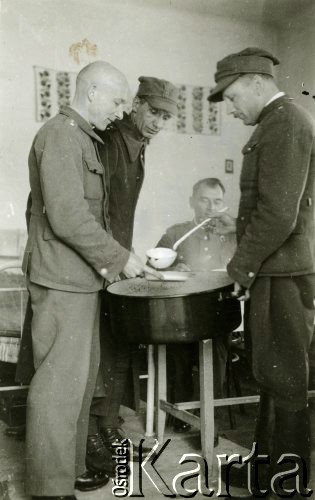 1940, Targu-Jiu, Rumunia
Obóz internowania dla żołnierzy Wojska Polskiego, wydawanie obiadu; stoją od prawej: podporucznik w mundurze polowym wz. 36 i w rogatywce polowej wz. 37 - oficer ten chochlą nalewa z garnka zupę, z tyłu siedzi kpt. pilot Tadeusz Krajewski, w środku stoi porucznik w mundurze - płaszczu polowym wz. 36 i w rogatywce polowej wz. 37, z lewej podporucznik w mundurze polowym wz. 36. Na odwrocie pieczątka Oflag VI/B Geprüft 7a.
Fot. NN, zbiory Ośrodka Karta, album (A-XII), udostępnił A. Krajewski.

[II wojna światowa, lata 40-te, Polacy w Rumunii, Targu Jiu, obóz internowania dla żołnierzy WP, Wojsko Polskie, obozy, internowanie, jeńcy, internowani, żołnierze, oficerowie, lotnictwo, lotnicy, lotnik, piloci, pilot, jedzenie, wyżywienie, zupa]