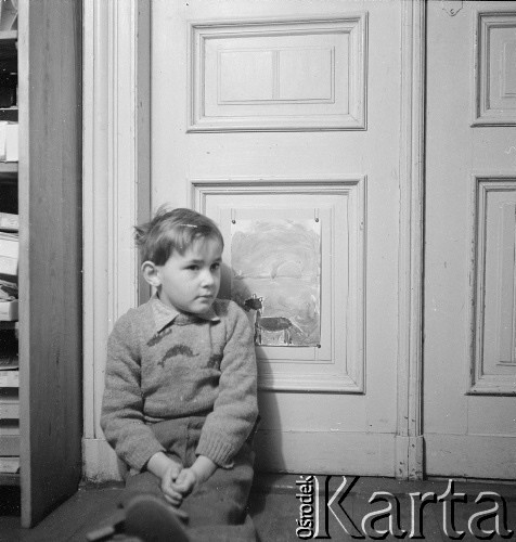 styczen 1954, Warszawa, Polska
Marek Jarosiński (syn Ireny Jarosińskiej)  siedzi pod drzwiami pracowni, w tle jego obrazki.
Fot. Irena Jarosińska, zbiory Ośrodka KARTA