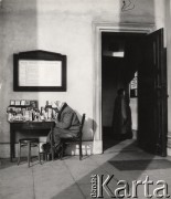 lata 50-te, Warszawa, Polska.
Kobieta pisząca przy stoliku z dewocjonaliami przed Kościołem św. Aleksandra na Placu Trzech Krzyży. Kobieta stojąca w drzwiach czyta kartkę: 