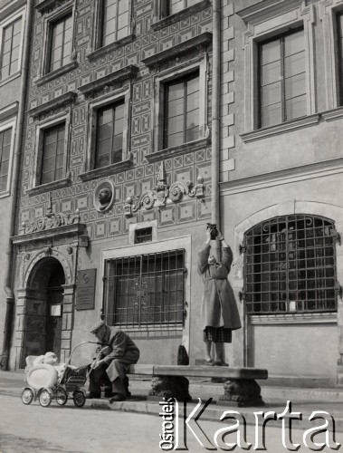 lata 50-te, Warszawa, Polska.
Kobieta fotografująca kamienice na rynku Starego Miasta. Na kamiennej ławie siedzi mężczyzna, pilnujący dziecka w wózku. W tle kamienica 