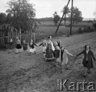 1961, Kadzidło, Polska.
Wieś kurpiowska. Wiejska droga. Kobieta w stroju kurpiowskim, za nię dzieci trzymające się za ręce.
Fot. Irena Jarosińska, zbiory Ośrodka KARTA