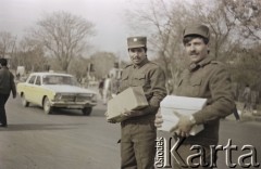 1992, Kabul, prowincja Kabul, Afganistan.
Dwaj żołnierze niosą pakunki. Za nimi, na ulicy radziecki samochód osobowy marki 