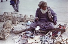 1992, Kabul, prowincja Kabul, Afganistan.
Targ uliczny na bulwarach nad rzeką Kabul. Szewc naprawia buty. Obok niego leżą przeznaczone na sprzedaż klatki dla ptaków. 
Fot. Irena Jarosińska, zbiory Ośrodka KARTA