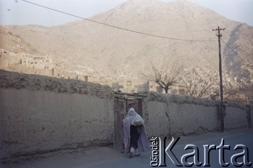 1992, Kabul, prowincja Kabul, Afganistan.
Kobieta w burce i młoda dziewczyna idą poboczem drogi. W oddali widoczne osiedle domów u podnóża Wzgórz Asmai.
Fot. Irena Jarosińska, zbiory Ośrodka KARTA