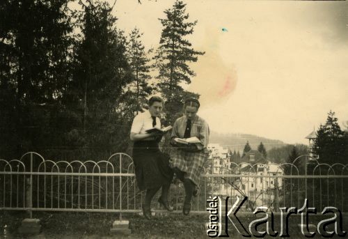 14.04.1940, Baile Govora, Rumunia.
Dwie młode kobiety siedzące na ogrodzeniu i czytajace książki, w tle fragment miasteczka; podpis na odwrocie: 