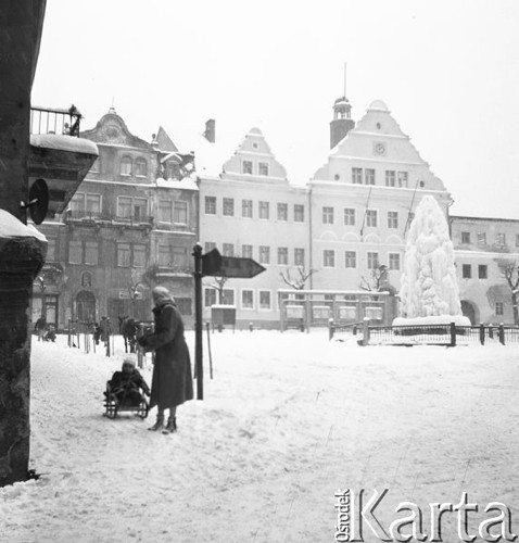 Luty 1956, Polska.
Rynek miasta zasypany śniegiem, z lewej kobieta ciągnąca dziecko na sankach.
Fot. Romuald Broniarek, zbiory Ośrodka KARTA