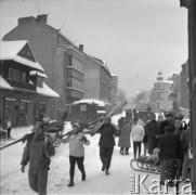 Luty 1957, Zakopane, Polska.
Troje narciarzy z nartami na ramionach idzie zaśnieżoną ulicą, z prawej dziecko na sankach.
Fot. Romuald Broniarek, zbiory Ośrodka KARTA