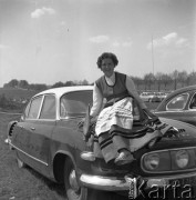 Maj 1958, Polska.
Kobieta w ludowym stroju siedzi na masce samochodu marki 