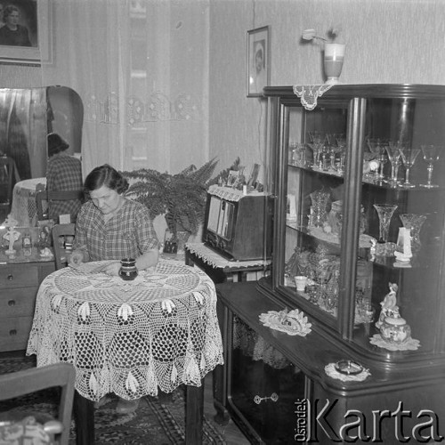 Październik 1958, Warszawa, Polska.
Kobieta siedzi przy stoliku przykrytym białym obrusem, z prawej serwantka z kieliszkami i kryształami.
Fot. Romuald Broniarek, zbiory Ośrodka KARTA