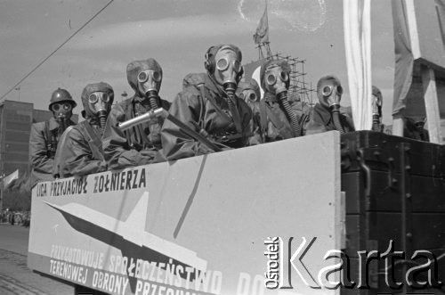 1.05.1959, Warszawa, Polska. 
Obchody święta 1 Maja, pochód przechodzący ulicą Marszałkowską, na pierwszym planie mężczyźni w kombinezonach i maskach gazowych jadący na przyczepie  z napisem: 