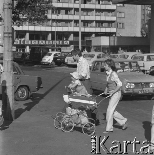 Maj 1977, Warszawa, Polska.
Fragment miasta, młoda kobieta z dzieckiem w wózku przechodząca przez ulicę, w tle samochody parkujące na chodniku.
Fot. Romuald Broniarek/KARTA