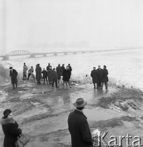 Styczeń 1966, Wyszogród, Polska.
Grupa osób obserwuje Wisłę skutą lodem, w tle drewniany most na rzece.
Fot. Romuald Broniarek/KARTA