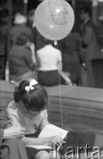Maj 1967, Warszawa, Polska.
Kiermasz książki przed Pałacem Kultury i Nauki, na zdjęciu dziewczynka z balonikiem czyta książkę.
Fot. Romuald Broniarek/KARTA