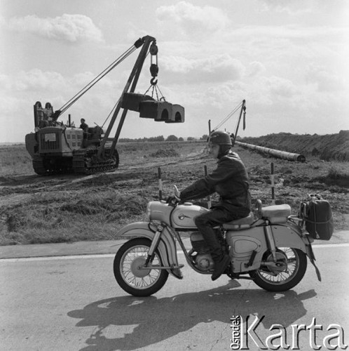 Wrzesień 1967, Lipsk (okolice), Niemiecka Republika Demokratyczna (NRD)
Polscy robotnicy z przedsiębiorstwa Hydrobudowa-6 budują rurociąg w okolicach Lipska, na pierwszym planie motocyklista jadący drogą.
Fot. Romuald Broniarek/KARTA
