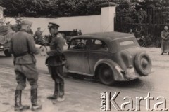 1940, Francja.
 Na pierwszym planie rozmawiają dwaj oficerowie Wehrmachtu. Na dalszym planie samochód Opel i inne samochody niemieckiej armii. Widoczny również żołnierz z jednostki kolarzy, przy bramie stoi motocyklista w długim płaszczy skajowym.
 Fot. NN, zbiory Ośrodka KARTA, udostępnił Stanisław Blichiewicz
   

