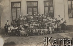 1935-1936, brak miejsca.
Przedszkole - grupa dzieci w asyście dorosłych kobiet. Na drugim planie widoczne są okna budynku przedszkola.
Fot. Józef Tarań, zbiory Ośrodka KARTA, kolekcję zdjęć przekazała Lucyna Kumiszczo