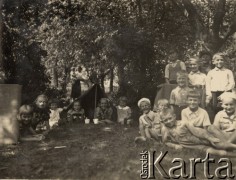 Brak daty, brak miejsca.
Grupa dzieci siedzących na leśnej polanie. Na drugim planie widoczne są dwie dziewczynki leżące w namiocie, w tle - kobieta z dzieckiem na ręku.
Fot. Józef Tarań, zbiory Ośrodka KARTA, kolekcję zdjęć przekazała Lucyna Kumiszczo