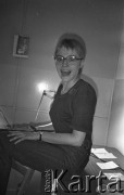 25.06.1981, Radom, Polska.
Kobieta w okularach siedząca na blacie stołu. Na ścianie zawieszona została reprodukcja obrazu Leonarda da Vinci zatytułowanego 