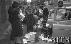 25.06.1981, Radom, Polska.
Grupa osób ogląda zawartość pudeł wyjętych z samochodu osobowego. W tle - zaparkowane samochody oraz fragment namalowanego na bloku napisu: 