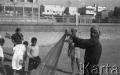 1943, Bliski Wschód.
Dzieci na plaży, z prawej stoi mężczyzna trzymający sieć rybacką. W tle fragment miasta.
Fot. Czesław Dobrecki, zbiory Ośrodka KARTA, Pogotowie Archiwalne [PAF_015], przekazał Krzysztof Dobrecki
