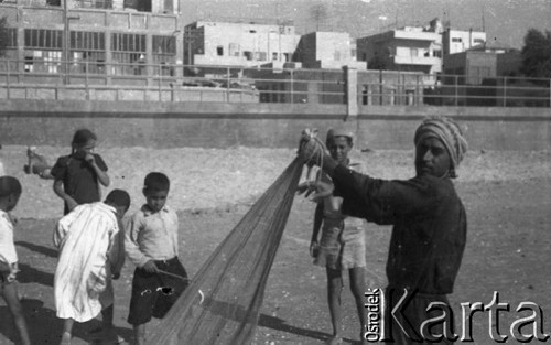 1943, Bliski Wschód.
Dzieci na plaży, z prawej stoi mężczyzna trzymający sieć rybacką. W tle fragment miasta.
Fot. Czesław Dobrecki, zbiory Ośrodka KARTA, Pogotowie Archiwalne [PAF_015], przekazał Krzysztof Dobrecki

