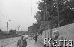 Sierpień 1980, Gdańsk, Polska.
Strajk okupacyjny w Stoczni Gdańskiej im. Lenina. Przechodnie przechodzą przy murze otaczającym stocznię. Na słupie wisi flaga oraz tablica z hasłem 