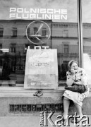 1982, Kraków, Polska.
Kobieta w chustce na głowie siedzi przed siedzibą LOT-u. Obok niej reklama i dziecięce buty.
Fot. Jerzy Szot, zbiory Ośrodka KARTA