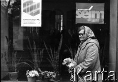 Październik 1985, Kraków, Polska
Kampania wyborcza przed wyborami do parlamentu. Kobieta handlująca kwiatami stoi przed budynkiem. W oknie wiszą plakaty z hasłami: 