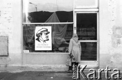 Październik - listopad 1988, brak miejsca, Polska
Kobieta przed sklepem z tkaninami. Na oknie sklepu wisi plakat z wizerunkiem Włodzimierza Lenina oraz napisem: 