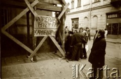 1989, Polska.
Przechodnie oglądają plakat przypięty do rusztowania z napisem 