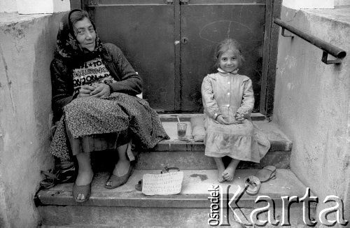 1992, Kraków, Polska.
Kobieta i dziewczynka siedzą na schodach domu przy uL Św. Tomasza. Kobieta prosi o pieniądze, trzymając przed sobą tekturową kartkę z napisem 