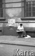 1990, Wrocław, Polska.
Kampania wyborcza przed wyborami samorządowymi. Kobieta siedząca przed budynkiem, obok wisi transparent o treści: 