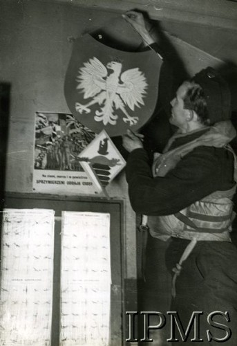1940-1943, Wielka Brytania.
Plut. Jan Pomietlarz z dywizjonu 306 wiesza polskie godło na ścianie, poniżej odznaka dywizjonu. W tle wisi plakat 