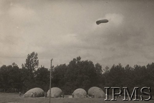 Lata 20., Polska.
Biwak balonów zaporowych. Przygotowanie do wzlotu balonu zaporowego „NN” (górny). W 1924 r. warsztat powłokowy Centralnego Zakładu Balonowego w Legionowie uruchomił produkcję pierwszych w Polsce balonów zaporowych „N”-„NN”, których licencję zakupiono we Francji. Ich szycie rozpoczęto na początku sierpnia 1924 r.   Balony „N”-„NN”, systemu „Caquot DCA” (Defense Contre Aeronefs – OPL), skonstruował francuski oficer – mjr inż. Albert Caquot. Balony były używane po dwa. W celu zwiększenia pułapu operacyjnego łączono je w tandem (jeden nad drugim), połączony stalową liną. Teoretycznie osiągał on pułap 4500 m, ale w rzeczywistości po uwzględnieniu kąta znoszenia był niższy o 700 m. Balon „NN” (górny) o długości 17,3 m osiągał objętość ok. 288 m³. Balony „N”-„NN” były ówcześnie jednymi z najnowocześniejszych na świecie. Mjr A. Caquot zastosował w nich nietypowy sposób wyrównywania gazu w powłoce, którego objętość rozszerzała się wraz z wysokością. W tym celu wbudował w powłokę, widoczny na powyższym zdjęciu, gumowy pas rozszerzalny.
Album balonowowy - fotografie po dr Niedźwierskim.
Fot. NN, Instytut Polski im. Gen. Sikorskiego w Londynie