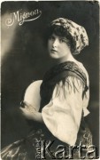 Pocz. XX wieku, Francja.
Portret kobiety w stroju ludowym - w spódnicy, białej bluzce, dwóch kwiecistych chustach, w białym czepku z elementami kwiatów i liści na głowie. Kobieta trzyma w dłoniach tamburyn. Zdjęcie wykonane w atelier fotograficznym. Na zdjęciu podpis: 