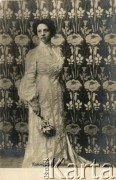 Pocz. XX wieku, Rosja.
Portret kobiety w białej sukni, z pękiem kwiatów w prawej dłoni, na tle ciemnej tapety w jasne kwiaty. Zdjęcie wykonane w atelier fotograficznym. Napis na pocztówce w języku rosyjskim.
Fot. NN, zbiory Ośrodka KARTA, kolekcja Ryszarda Łopatki