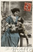 Ok. 1907, Francja.
Portret kobiety w niebieskiej sukni oraz jej syna w garniturze z krótkimi spodniami, siedzących na ławce i wpatrzonych w siebie. Na kolanach kobiety leży koszyk z kwiatami. Zdjęcie wykonane w atelier fotograficznym. Napis pod fotografią: 