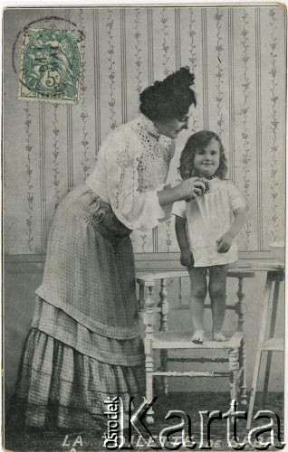 1900-1924, Francja.
Portret kobiety w białej bluzce i kraciastej spódnicy, myjącej dziewczynkę w podomce, stojącą boso na krześle. Napis na kartce w języku francuskim: 