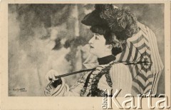 Pocz. XX wieku, Paryż, Francja.
Portret kobiety w sukni, z ozdobnym kapeluszem, trzymającej w dłoni parasolkę w biało-czarne pasy. Zdjęcie wykonane w atelier fotograficznym. Karta sygnowana nazwiskiem fotografa 