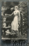 Pocz. XX wieku, Warszawa, zabór rosyjski.
Portret młodej pary - kobiety w sukni i mężczyzny w ciemnym garniturze i kapeluszu. Zdjęcie wykonane w atelier fotograficznym. Podpis pod zdjęciem: 