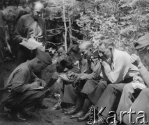 1942-1944, Münchenbuchsee, Szwajcaria.
Żołnierze 2. Dywizji Strzelców Pieszych odpoczywają w trakcie ćwiczeń polowych w lesie. Jeden z żołnierzy robi zdjęcie oficerowi, który na kolanach zapisuje notatki.
Fot. Jerzy Konrad Maciejewski, zbiory Ośrodka KARTA 
